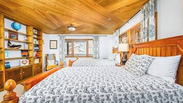 A bedroom with a large bed, wooden headboard, a bookshelf, and a window with curtains.