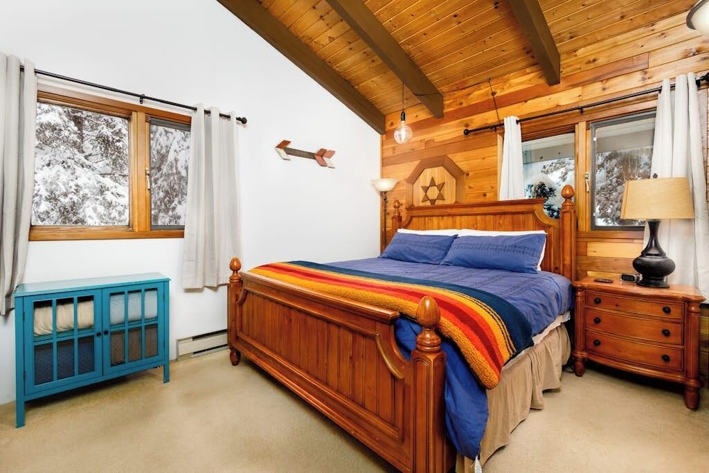 Una camera da letto in legno con un letto, comodini e una finestra con tende.