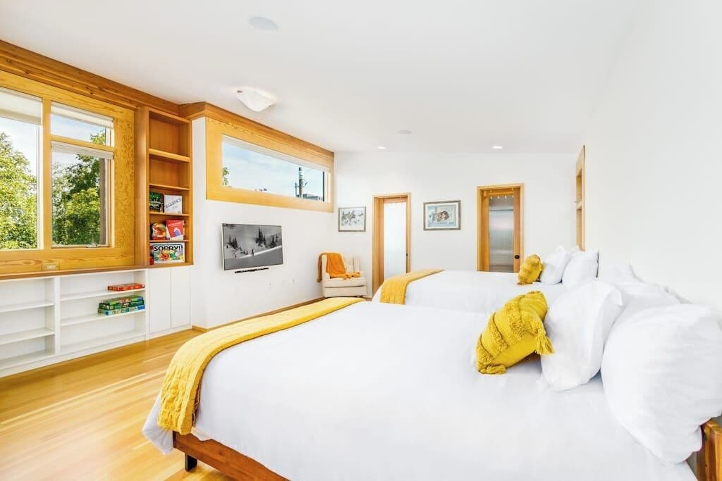 A modern bedroom with a large bed, a wooden headboard, a built-in TV, and a window with a view of greenery.