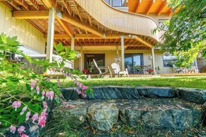A modern house with a curved wooden deck, outdoor seating, and a garden with flowering plants. - Award-winning Anchorage Kitchen w/ Cook Inlet Views (Anchorage)