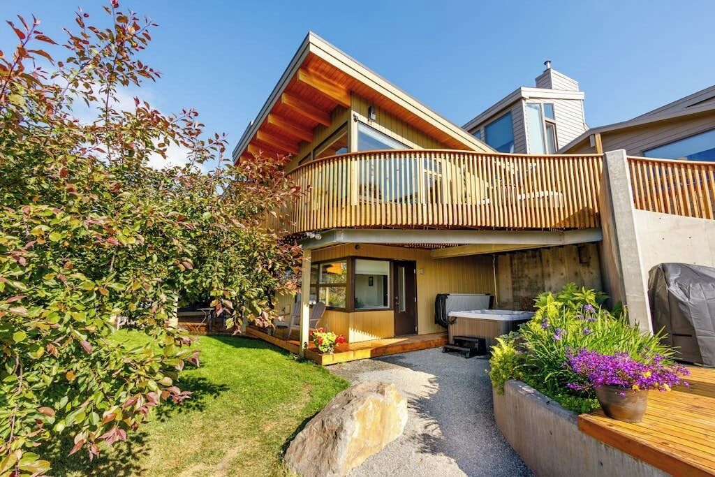A modern two-story house with a balcony, a patio area, and a garden.