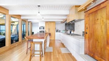 A modern kitchen with wooden flooring, white cabinetry, and a central island with stools.