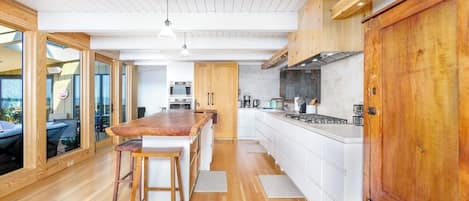 A modern kitchen with wooden flooring, white cabinetry, and a central island with stools.
