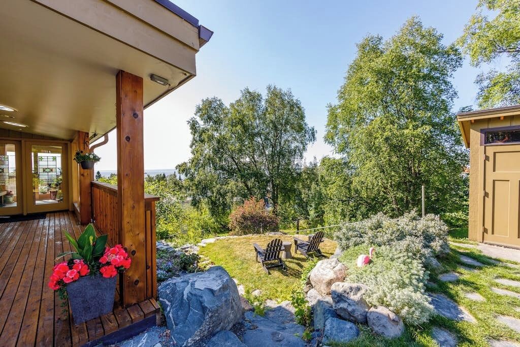 A wooden deck with a covered area, outdoor seating, and a garden with rocks and plants.