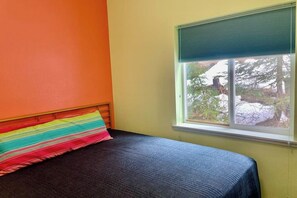 A bed with a colorful striped pillow, a window with a view of trees and a building, and a wall painted in two colors.