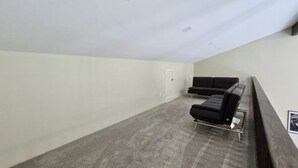 Um quarto com carpete cinza, sofá preto e uma porta.