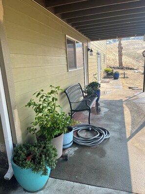 A covered porch with potted plants, a bench, and a hose on the ground.