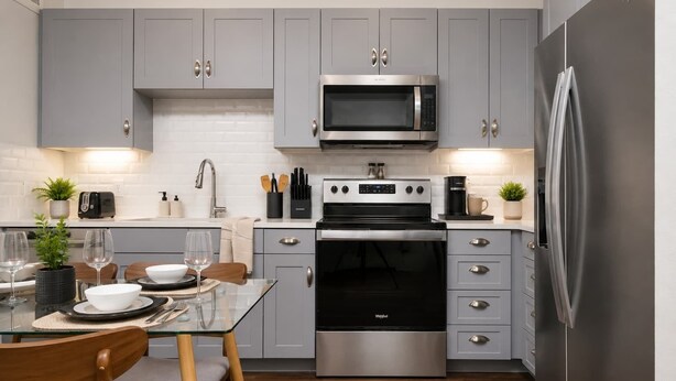 A modern kitchen with grey cabinets, stainless steel appliances, and a glass dining table. - Sleek Haven Suite  | Pool • Gym • Parking | Downtown San Antonio (San Antonio)