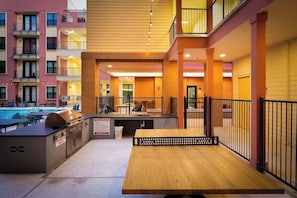 An outdoor patio area with a wooden table, barbecue grill, and poolside seating. - Sleek Haven Suite, Pool, Gym, Parking, Downtown San Antonio (San Antonio)