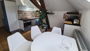 Une cuisine compacte avec un mur recouvert de carreaux, un coin repas avec des chaises blanches et une petite table.