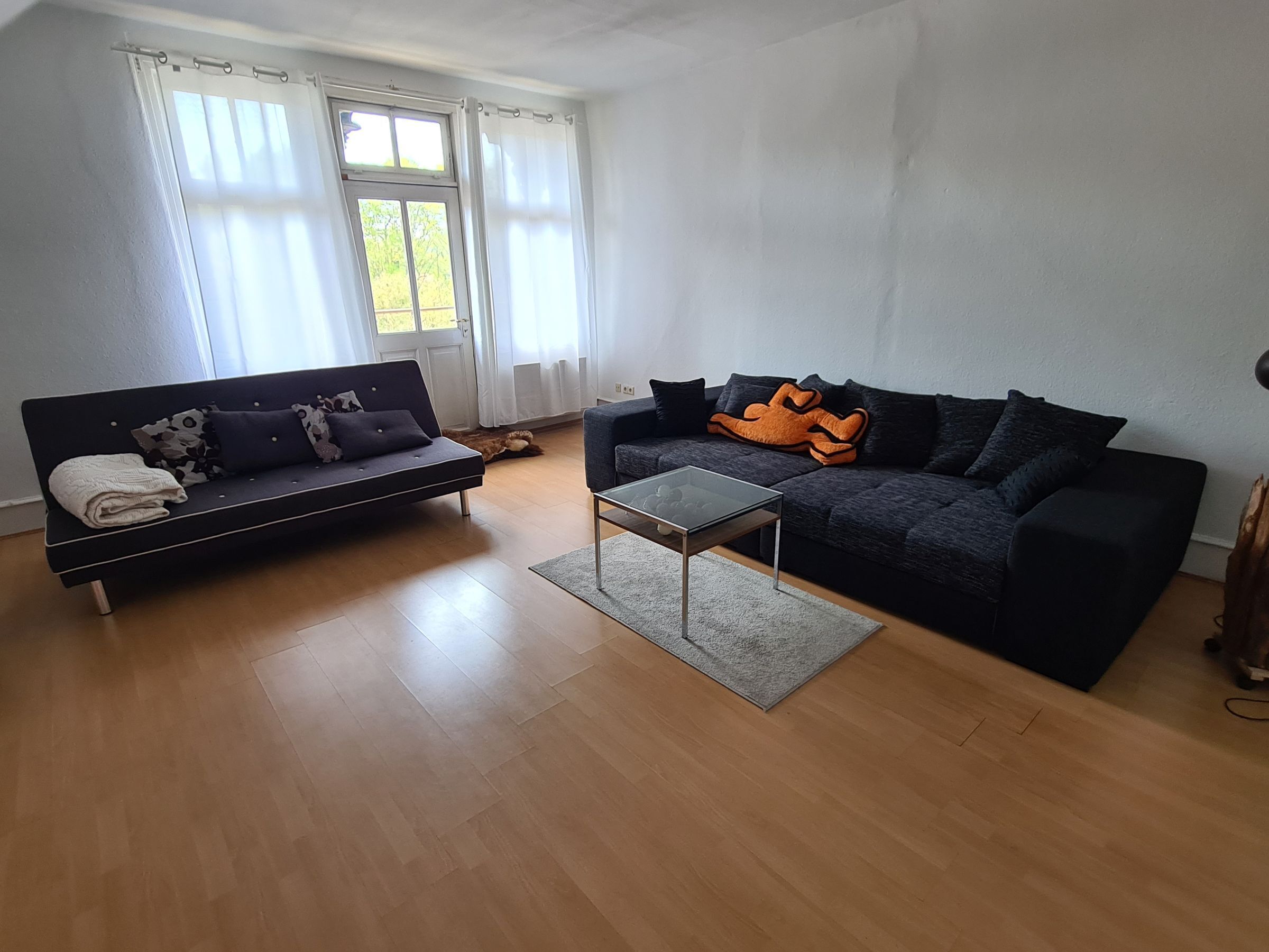 Ein Wohnzimmer mit zwei Sofas, einem Couchtisch und einem Fenster mit Vorhängen.