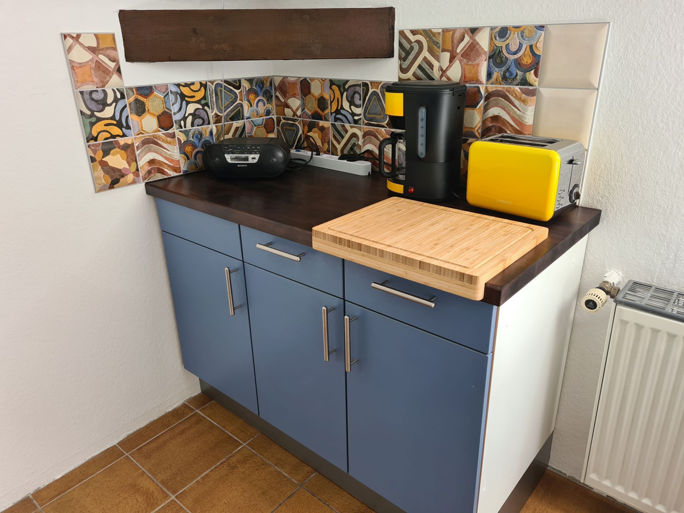 Une cuisine équipée d’une machine à café, d’un grille-pain et d’une planche à découper posée sur le plan de travail.