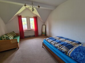 A bedroom with a sloped ceiling, a bed with a patterned bedspread, a wicker chair, and a large mirror. - Villa in Adelsheim - Historischer Charme im Herzen von Adelsheim (Adelsheim)