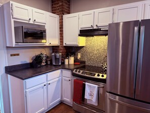 A kitchen with white cabinets, a stainless steel refrigerator, a microwave, and a coffee maker.