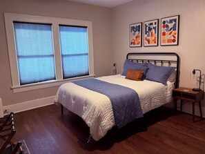 A bedroom with a bed, a nightstand, a lamp, and a window with blinds.
