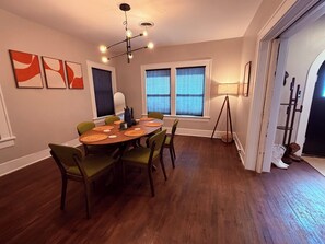 A dining area with a round table, green chairs, and a modern chandelier.