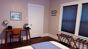 Un dormitorio con cama, escritorio, silla, ventana con persianas y puerta.