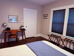Ein Schlafzimmer mit Bett, Schreibtisch mit Stuhl, Fenster mit Jalousien und einer Tür.