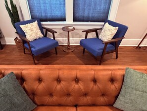 A room with a tufted orange sofa, two blue armchairs with white cushions, a small round wooden table, and a potted plant.