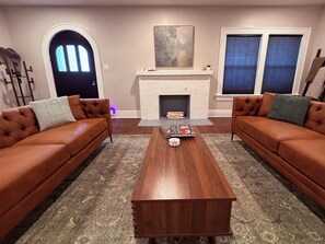 A living room with two brown leather sofas, a wooden coffee table, a fireplace, and a large painting on the wall. - Historic 1914 Texas Tudor: Walk to TTU Campus (Lubbock)
