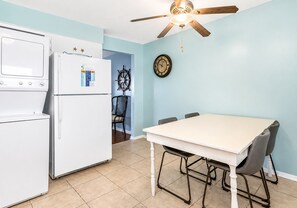A compact kitchen with a refrigerator, a stove, and a dining table with chairs. - Gulf View 17: Steps to Beach, Walk to The Hangout, Pool, Pet-Friendly (Gulf Shores)
