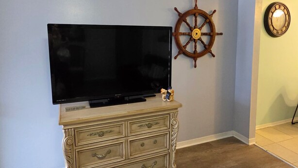 Una habitación con un televisor de pantalla plana sobre un aparador de madera, una rueda de barco en la pared y un reloj.