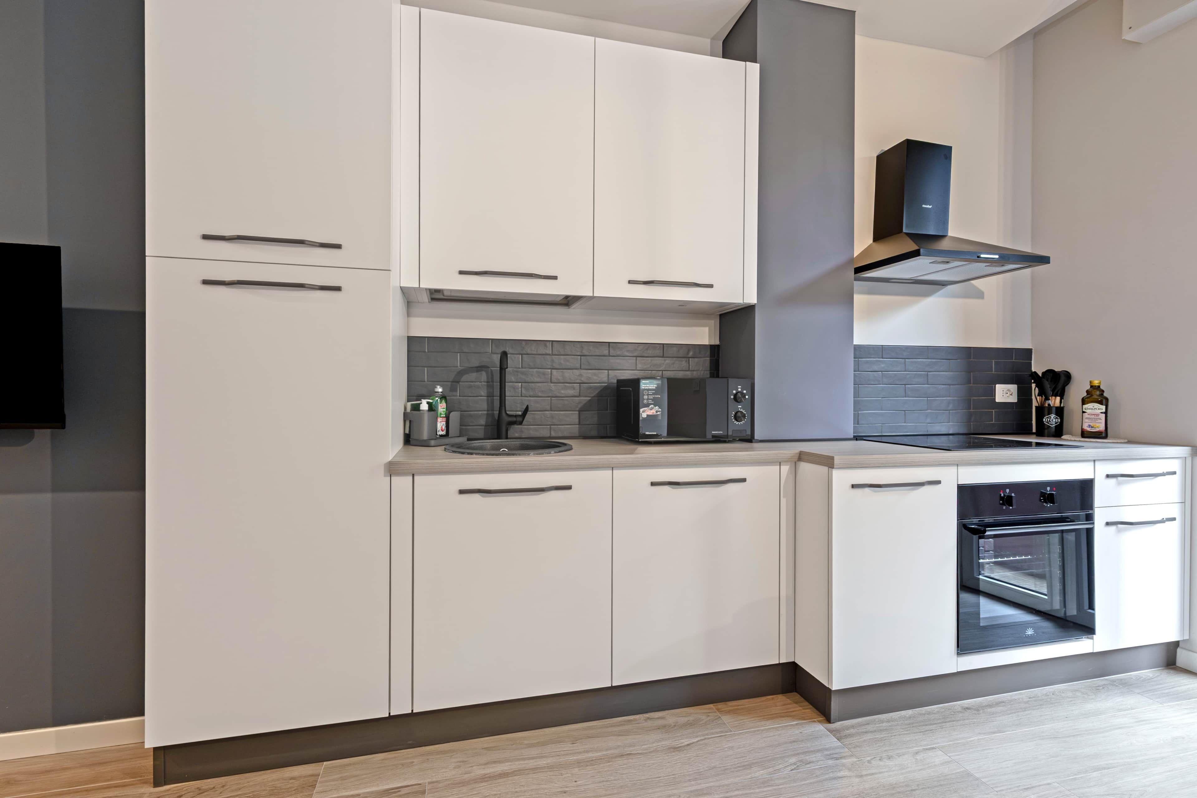 A modern kitchen with white cabinetry, a built-in oven, and a range hood.