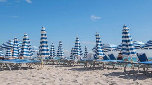 Ein Strand mit gestreiften Sonnenschirmen und Liegestühlen.