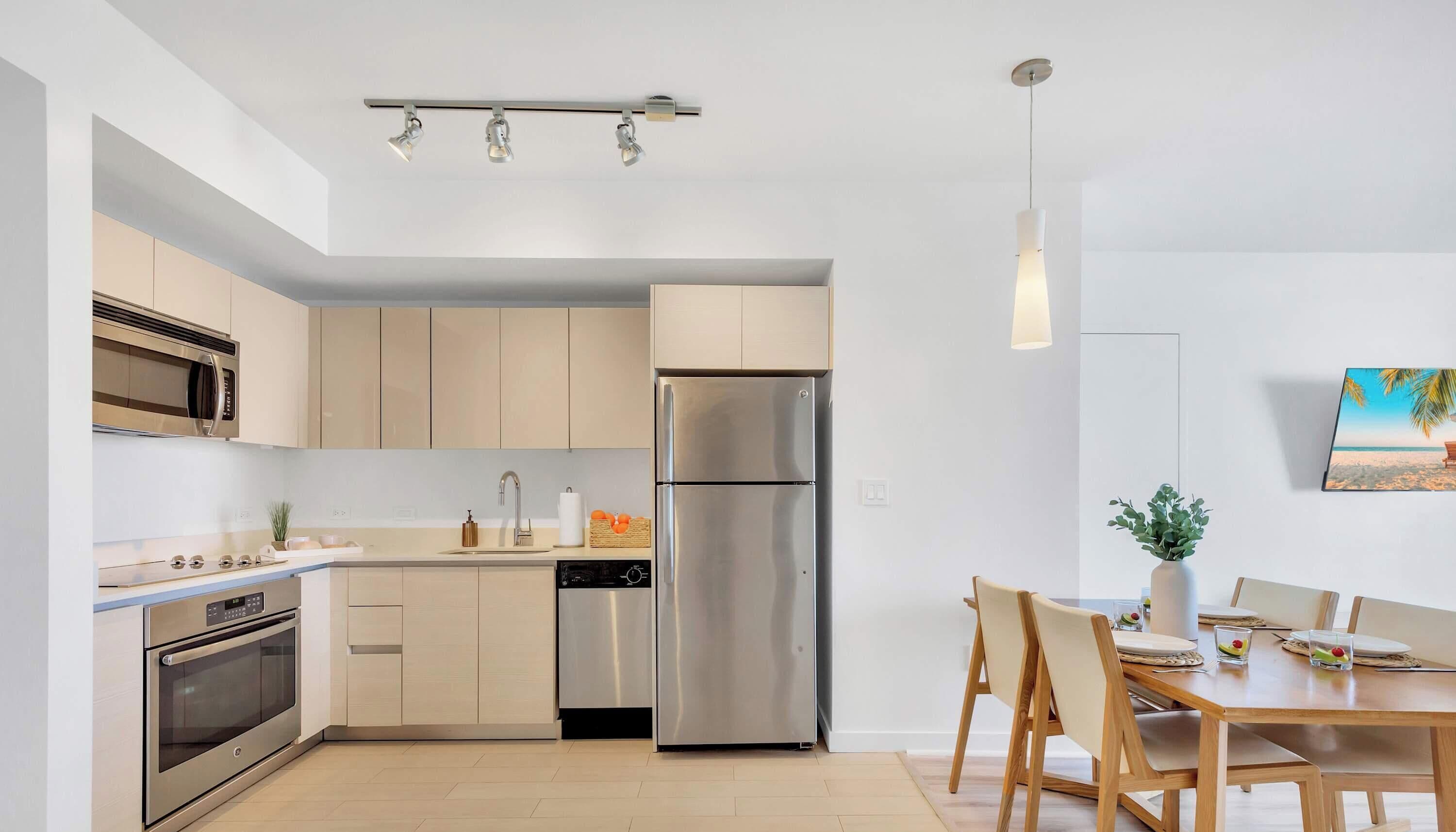 Una cocina moderna con electrodomésticos de acero inoxidable, un comedor con mesa y sillas de madera, y una lámpara colgante.