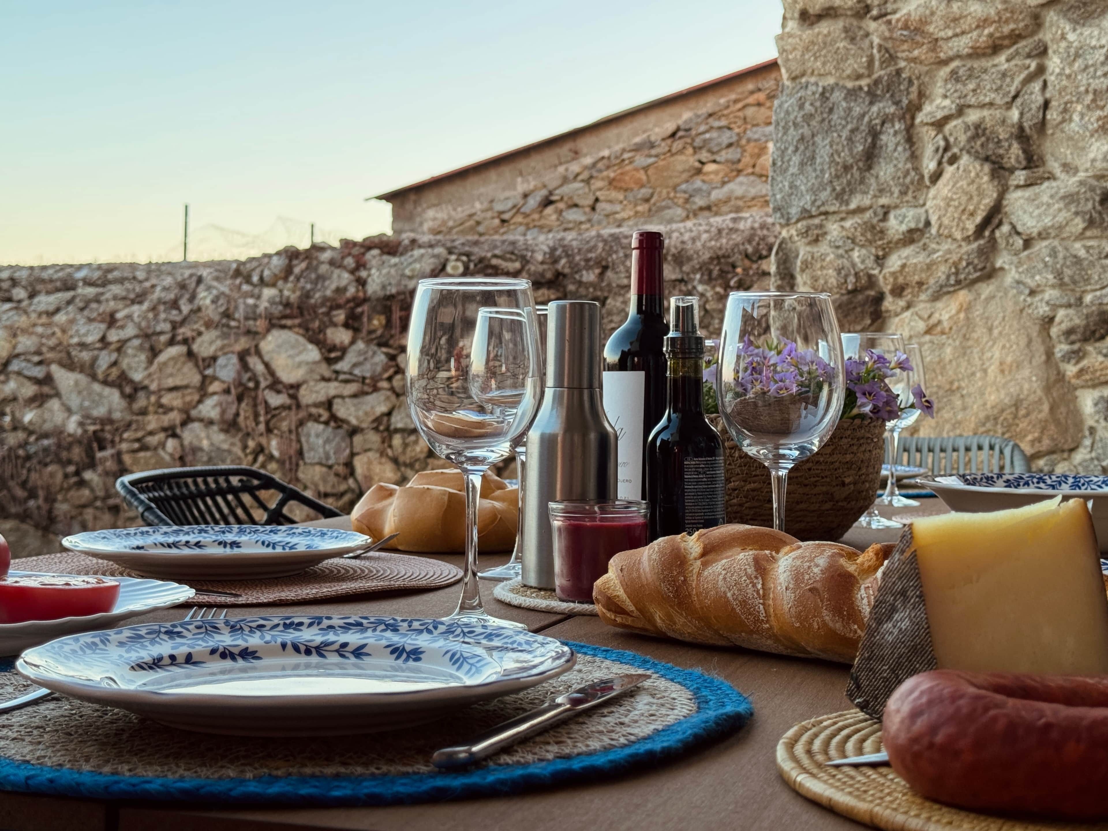 A table set for a meal with plates, cutlery, a bottle of wine, a loaf of bread, and a cheese wedge.