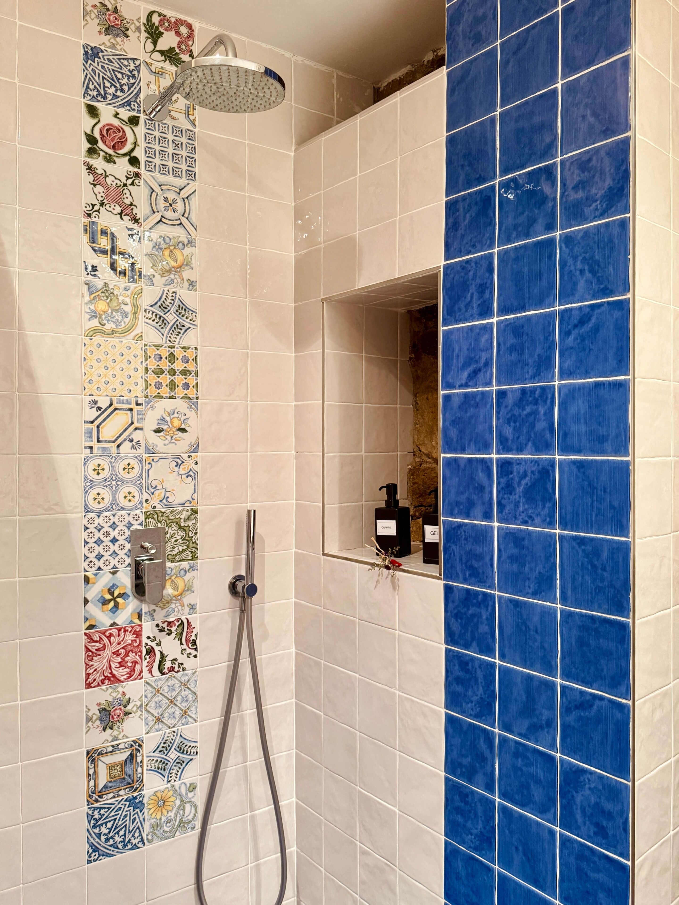 Un baño con ducha, secamanos y un espejo con repisa y artículos de aseo.