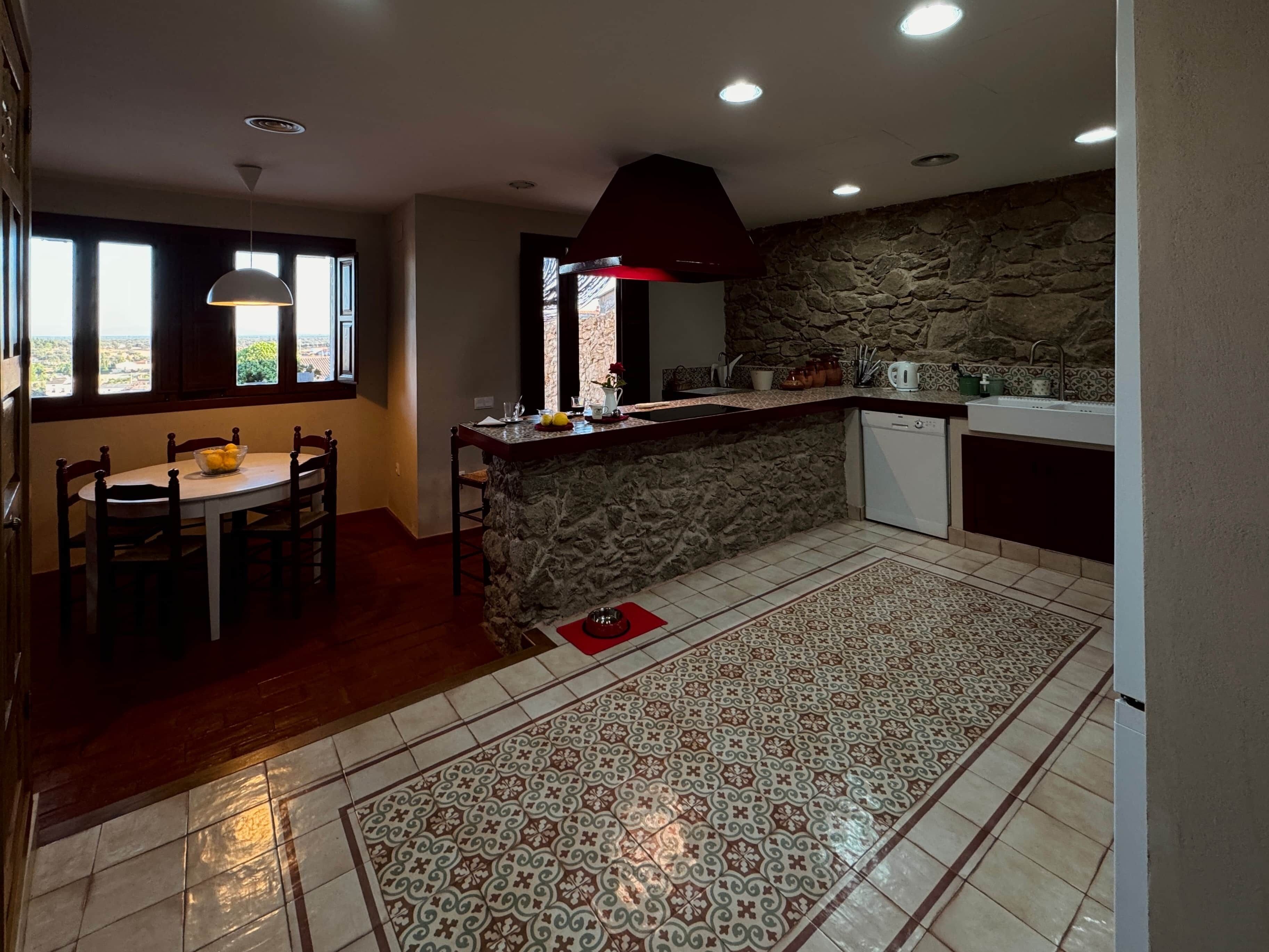A kitchen with a stone wall, a dining table with chairs, and a red rug.