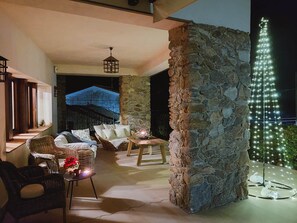 An outdoor seating area with wicker furniture, a stone wall, and a decorative light installation.