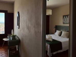 Ein Hotelzimmer mit Bett, Schreibtisch, Sessel und einer Zimmerpflanze, mit Blick auf die Stadt.