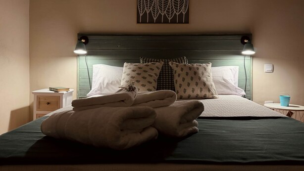 A neatly made bed with a dark green bedspread and white pillows, a bedside table with a book, and a wall-mounted artwork. - Las Pazuelas, the perfect rural getaway (Parrillas)