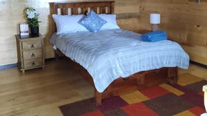 Ein Schlafzimmer einer Holzhütte mit einem Bett, einem Nachttisch, einer Lampe und einem farbenfrohen Teppich.