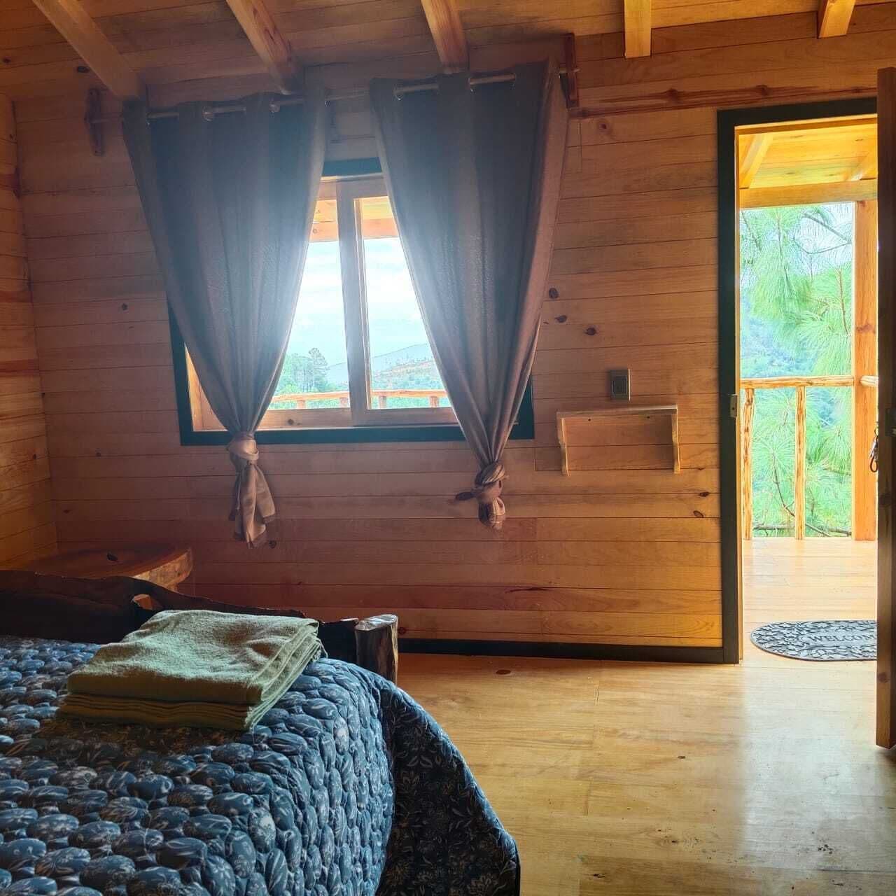Una habitación de cabaña de madera con cama, cortinas, una ventana y una puerta que da al exterior.