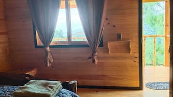 Una habitación de cabaña de madera con cama, cortinas, una ventana y una puerta que da al exterior.