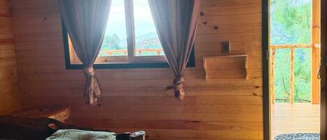 Una habitación de cabaña de madera con cama, cortinas, una ventana y una puerta que da al exterior.