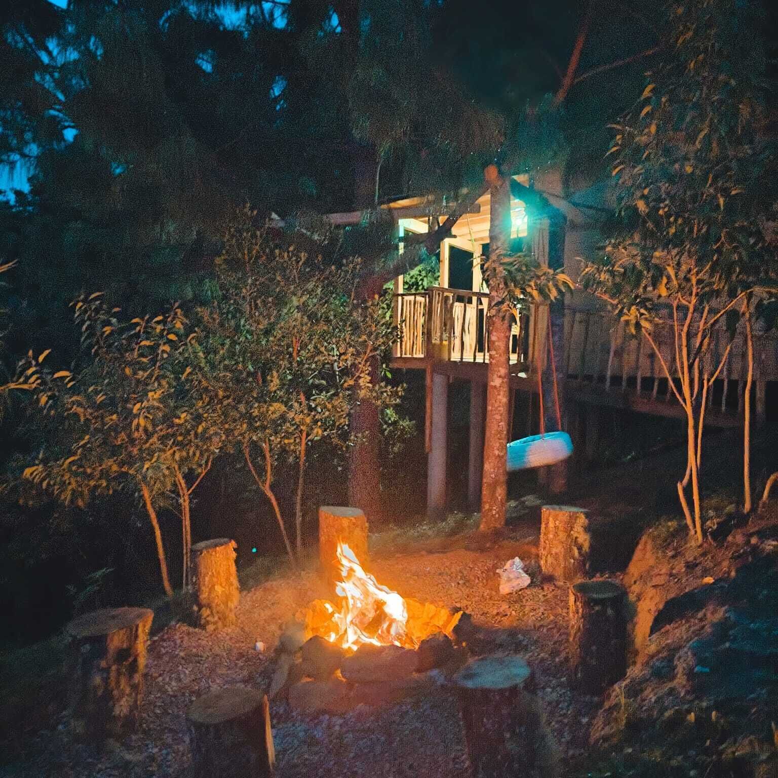 A wooden deck with a fire pit in the center, surrounded by trees and a building with a balcony.