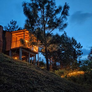 Una cabaña de madera con balcón, rodeada de árboles y una ladera.