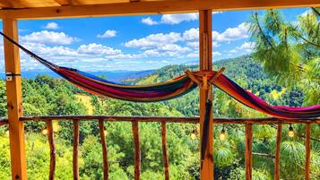A hammock suspended between wooden beams with a view of a lush green landscape.