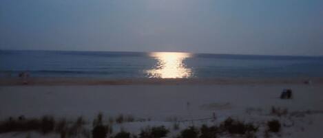 A beach with a clear sky, a visible sun, and a sandy shore.