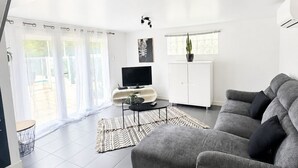 Ein modernes Wohnzimmer mit grauem Sofa, einem Flachbildfernseher, einem weißen Schrank und einem großen Fenster mit transparenten Vorhängen.