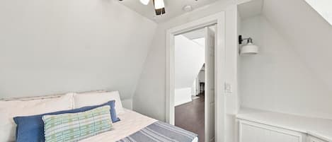 A bedroom with a bed, pillows, a ceiling fan, and a door leading to another room.