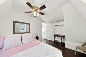 A bedroom with a bed, a ceiling fan, a mirror, a bedside table, and a chair. - The 1890 House where History meets the Horizon (Rockport)