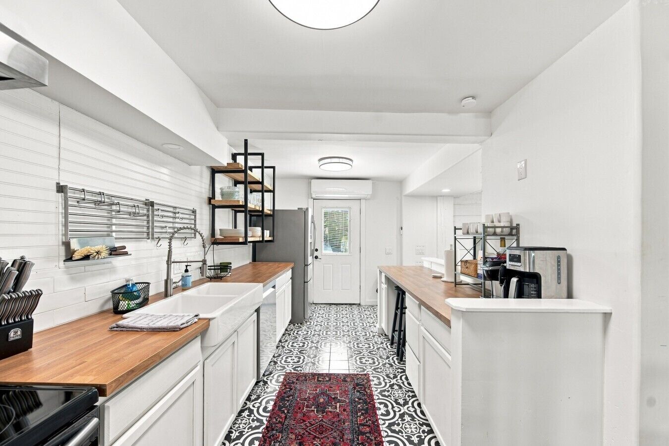 A modern kitchen with white cabinetry, a black and white patterned floor, and a red rug.