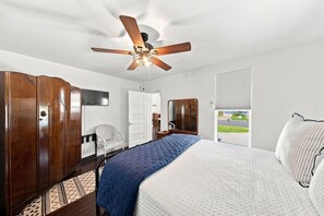 Ein Schlafzimmer mit Bett, Deckenventilator, Kleiderschrank, Stuhl und einem Fenster mit Blick.