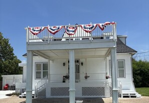 A two-story house with a balcony, white exterior, and a front porch with steps. - The 1890 House where History meets the Horizon (Rockport)