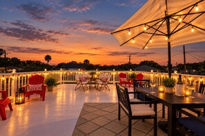 An outdoor patio with a table and chairs, string lights, and a sunset view. - The 1890 House where History meets the Horizon (Rockport)
